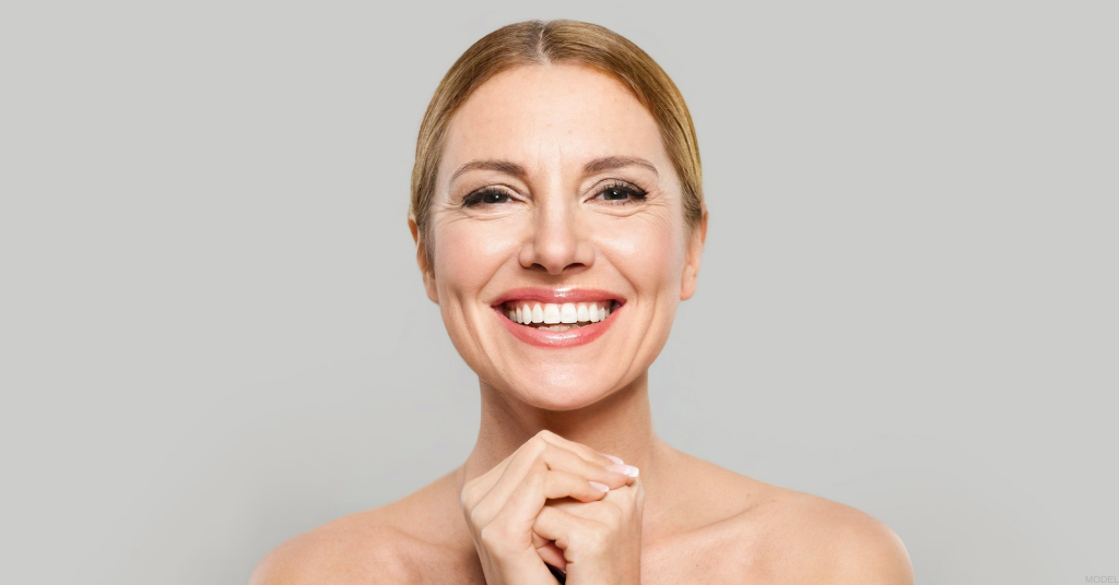 Woman smiling with hands clasped under her chin (model)